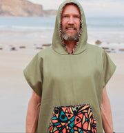 Man wearing a green hooded poncho with colorful pattern on a beach